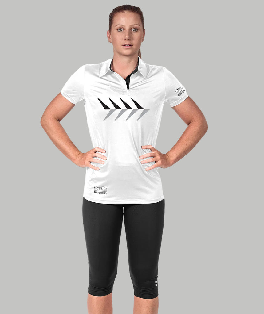 A woman wearing a white collared polo with black geometric patterns on the front, paired with black leggings. She is posing with her hands on her hips.